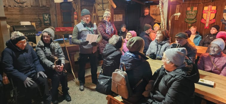 Ryhmä ihmisiä talvivaatteissa istuu pöytien ympärillä